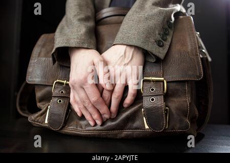 L'enseignant possède une vieille mallette en cuir marron, classique et avec boucles en métal, qui se tient sur une table noire. Gros plan. Banque D'Images