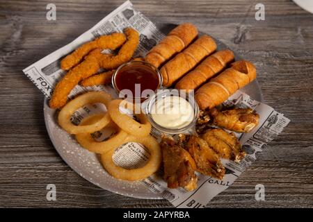 Plaque mixte de lanières de poulet, rondelles d'oignon, ailes de poulet et tequeños avec sauce sur fond en bois. Vue de dessus Banque D'Images