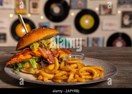 Hamburger maison avec poulet croustillant, bacon, guacamole avec sauce et frites sur table en bois. Image isolée. Banque D'Images