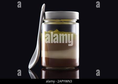 Dessert crème de lait en pot avec les noix, les fèves de cacao et chocolat isolé sur fond noir. Banque D'Images