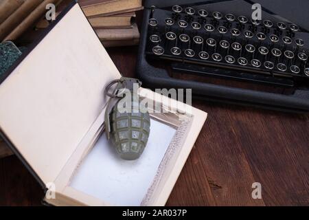 grenade à main cachée dans un livre avec ancienne machine à écrire rétro sur la terrasse en bois Banque D'Images