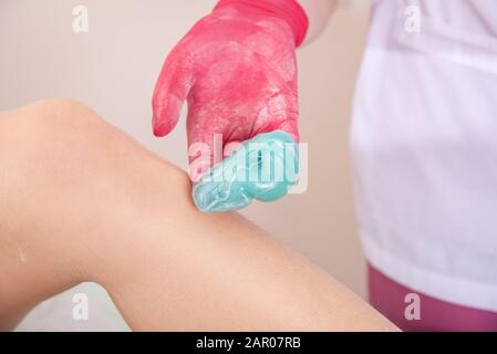 Le maître en gants médicaux rouges contient de la pâte liquide bleue pour l'épilation au sucre Banque D'Images
