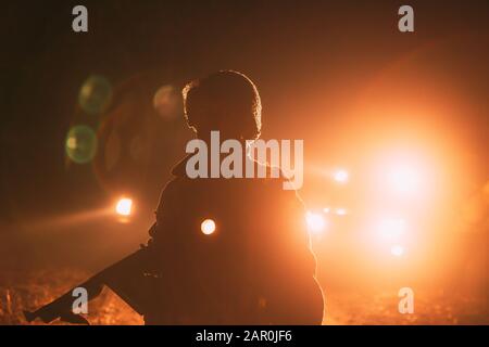 Réacteur Vêtu Comme Soldat De L'Infantry Of World War Ii Des Etats-Unis, Il Tient L'Arme De Sous-Machine Entre Les Mains. Portrait En Touche Bas. Lumière Des Véhicules Automobiles Feux Banque D'Images