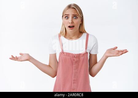 La jeune femme blonde, confuse et choquée, se déchit des étranges nouvelles, se haussant avec les mains se propageant sur le côté, se crachant les yeux et se dédrivant en essayant de la prouver Banque D'Images