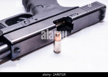 Un noir 9 mm semi-automatique avec sa lame ouverte avec une puce à pointe creuse de 9 mm à côté sur un fond blanc Banque D'Images