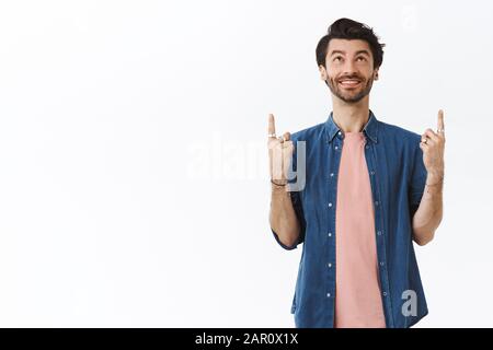 gaie gaie avec barbe, coiffure hipster, porter des bijoux, tenue moderne, regardant et pointant vers le haut amusant, sourire heureux, le check-out Banque D'Images