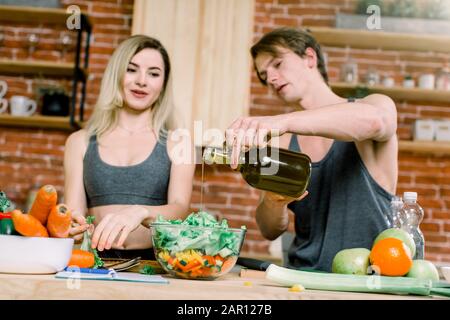 régime alimentaire, saine alimentation, forme physique style de vie, nutrition appropriée. santé conscient couple cuisine basse calorie dîner dans la cuisine à la maison. Un homme verse de l'huile d'olive Banque D'Images