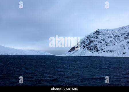 naviguer dans la neige couvrait les fjords norvégiens avec un petit bateau de pêche dans la distance finnmark norvège Banque D'Images