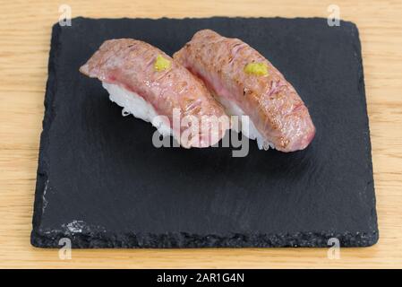 Nigiri de chaleur-gravé kobé habillés avec de la moutarde, servis sur une plaque carrée de l'ardoise, l'arrière-plan de table en bois Banque D'Images