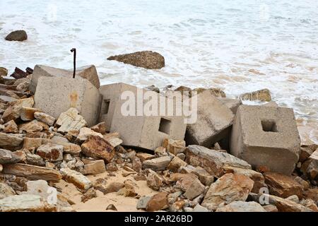 Blocs de béton laissés sur la rive couverte de roche et pierres au bord de la mer Banque D'Images