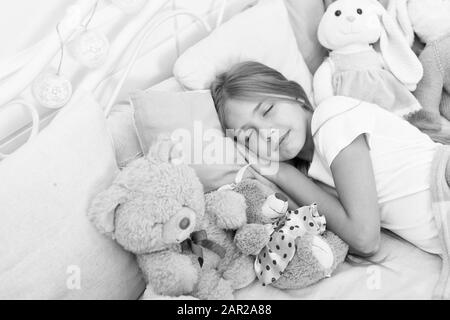 Jouer soft toy avant d'aller dormir. Dormir avec un jouet. L'insouciance de l'enfance. Se détendre avant de dormir. Soirée fille profiter de temps avec les jouets. Les enfants avec des jouets de lit oreiller couverture arrière-plan. Petite fille porter des pyjamas. Banque D'Images