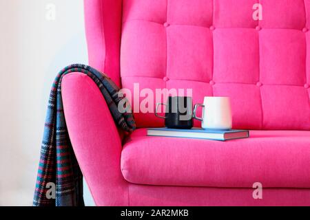 Tasse de thé et livre bleu sur un autocar rose avec couverture. Encore des détails de la vie dans la maison intérieure du salon. Intérieur confortable, concept de confort à la maison Banque D'Images