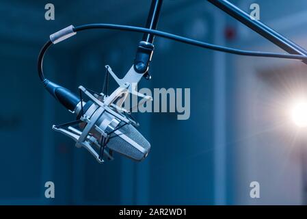 Un microphone à condensateur argenté professionnel monté sur un trépied noir installé dans une salle de concert avec éclairage d'ambiance. Banque D'Images