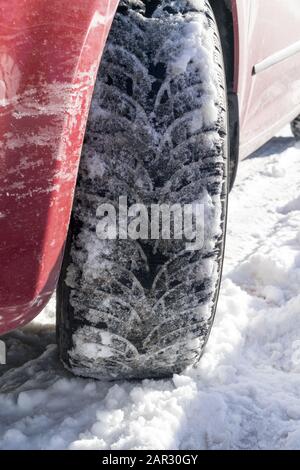 Voiture rouge avec pneus hiver sur une route enneigée, clôture, image verticale. Banque D'Images