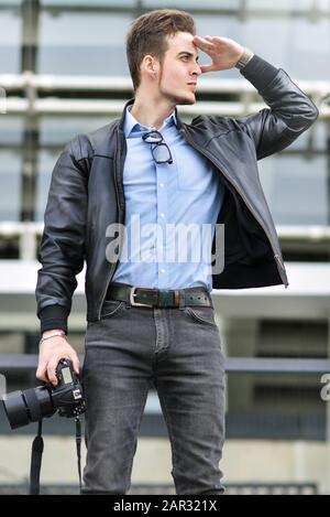 Adolescent prenant des photos à l'extérieur. Jeune homme travaille reporter, plein air. Le gars caucasien tient un appareil photo et capture de photos. Banque D'Images