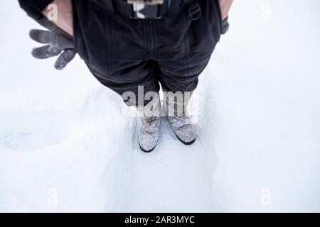 L'homme dans des bottes et des vêtements en feutre chaud se tient sur la piste, en arrière-plan de la neige, dans la cour. Vue de dessus. Banque D'Images