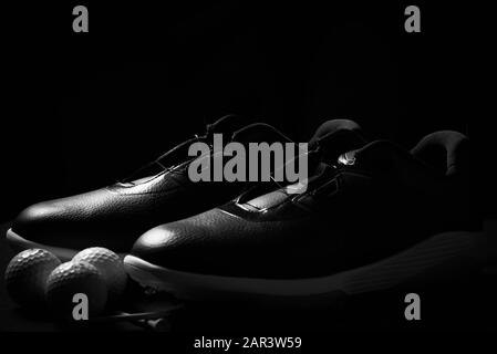 Chaussures de golf, balles et tee isolés sur fond noir. Banque D'Images