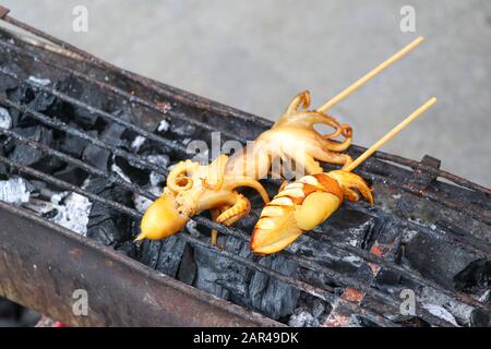 Brochette de calmars avec des bâtonnets grillés sur un poêle à charbon. Calmar grillé sur un poêle à charbon. Banque D'Images