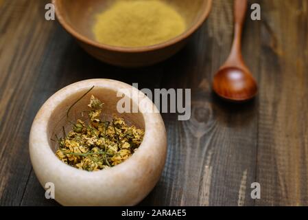 Mortier de marbre avec camomille séchée pour cosmétiques naturels. Bol en argile avec poudre jaune ou argile et fleurs sur fond en bois. Pose plate. Banque D'Images