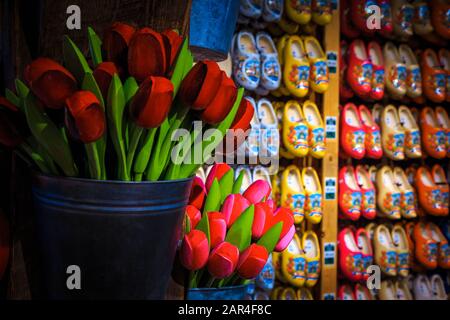 Des bouquets colorés de tulipes en bois dans le seau et des chaussures en bois en rangée sur le mur. Décoration de la boutique de souvenirs néerlandaise avec un objet cadeau fait main Banque D'Images