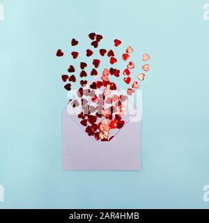 Petit confetti rouge en forme de coeur dans l'enveloppe sur fond bleu clair Banque D'Images