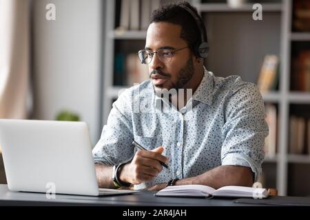 Un homme d'affaires africain concentré porte des écouteurs étudier en ligne regarder le webinaire Banque D'Images