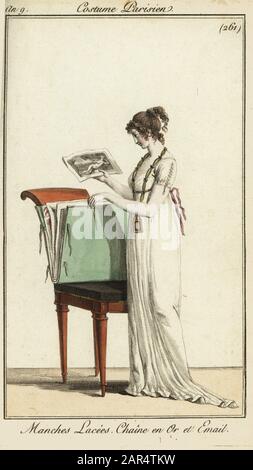 Femme regardant un portefeuille de gravures, 1800. Elle porte une robe unie avec manches lacées et une chaîne en or et émail. Manches lacées. Chîne en Ou et émail. Gravure en copperplate de couleur à la main du Journal des modes et Dames de Pierre de la Mesangere, Paris, 1800. Les illustrations du volume 4 étaient Carle Vernet, Bosio, Dutailly et Philibert Louis Debucourt. Banque D'Images