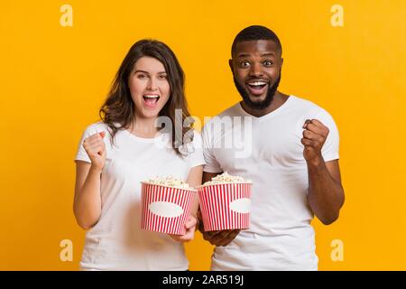 Un couple interracial joyeux qui applaudit avec des seaux à maïs soufflé, ce qui fait monter les poings dans l'excitation Banque D'Images