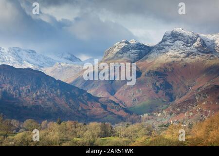 Le Langdale Pikes, Great Langdale, avec un dépoussiérage de neige en hiver avec des taches de nuages et de lumière dans le district de English Lake Banque D'Images