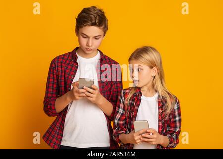 Image de la jeune femme espionnage et peeking sur smartphone de son petit ami isolé sur fond jaune Banque D'Images