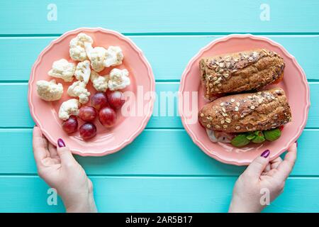 Mains féminines tenant deux assiettes et choisir la nourriture à manger entre les légumes ou sandwich, concept de régime alimentaire. Banque D'Images