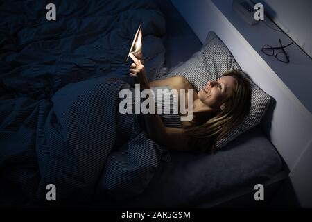 Jolie femme d'âge moyen, en utilisant son téléphone portable au lit avant de dormir Banque D'Images