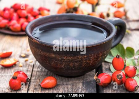 Teinture ou thé avec des hanches roses rouges dans une tasse en verre près des hanches roses sur une table en bois. Phytothérapie. Banque D'Images