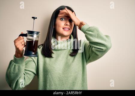 Jeune femme aux yeux bleus faisant du café à l'aide de la machine à café debout sur fond blanc stressé avec la main sur la tête, choquée avec la honte et surprise fa Banque D'Images