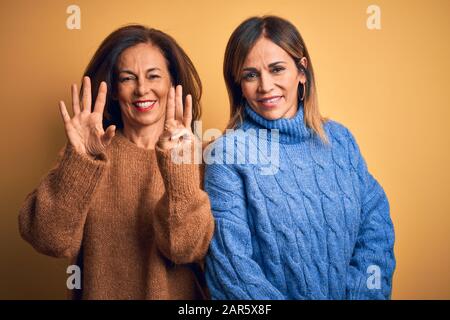 Âge moyen beau couple de sœurs portant un pull décontracté sur fond jaune isolé montrant et pointant vers le haut avec les doigts numéro huit pendant Banque D'Images