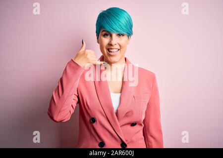 Jeune femme d'affaires avec des cheveux de mode bleu portant une veste sur fond rose souriant faisant un geste de téléphone avec la main et les doigts comme le talkin Banque D'Images