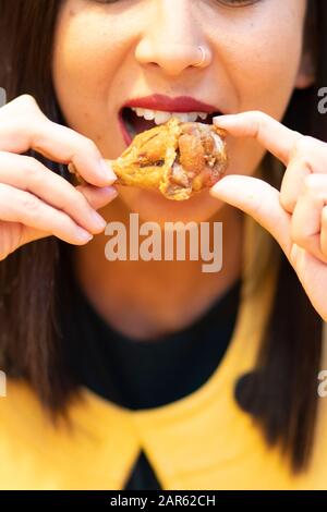 Jeune femme mangeant des ailes de poulet avec ses mains Banque D'Images