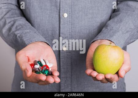 Les mains de l'homme tenant un lot de pilules et de capsules dans une main et la pomme dans l'autre. Banque D'Images