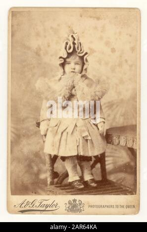 Carte de style victorien originale d'un jeune enfant mignon appelé Boogle (fille ou garçon vêtu de la même façon dans ces temps) portant un manteau d'hiver, avec un col en fourrure, et un capot élaboré, studio de A.G. Taylor, Londres, vers Royaume-Uni 1886 Banque D'Images