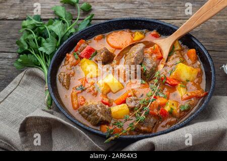 Goulash, ragoût de boeuf ou soupe de bogrash avec viande, légumes et épices dans la poêle en fonte sur table en bois. Cuisine hongroise. Style rustique. Banque D'Images