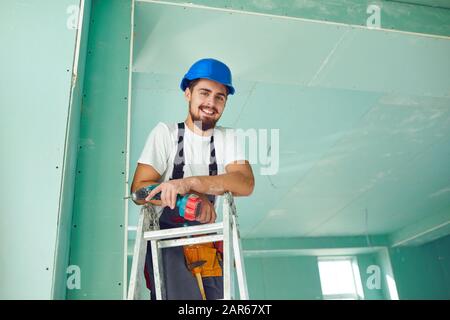 Un constructeur debout sur une échelle s'installe sur un site de construction de cloisons sèches Banque D'Images