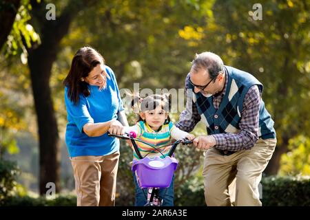 Grands-parents avec petite-fille apprenant à faire du vélo Banque D'Images