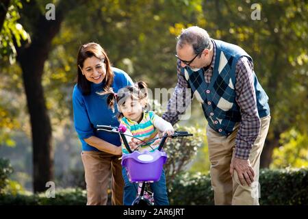 Grands-parents avec petite-fille apprenant à faire du vélo Banque D'Images