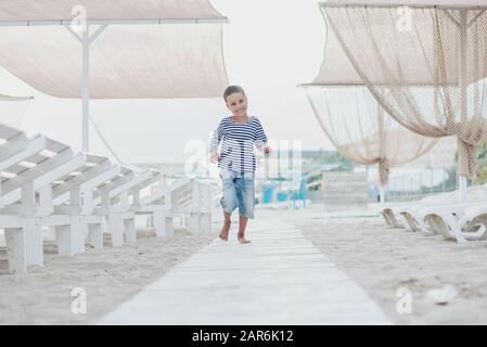 Garçon dans un T-shirt à rayures au bord de la mer. Enfant d'exécution sur la plage. Vacances d'été. Heureux enfant jouant sur la plage au coucher du soleil