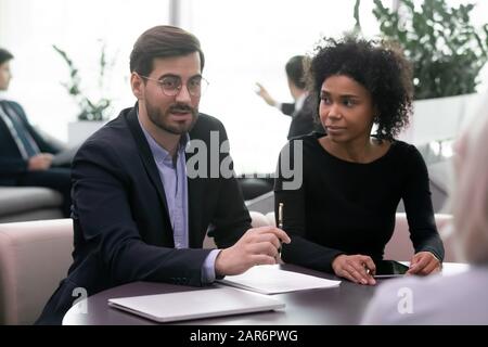 Assistant regardant un jeune homme d'affaires confiant discuter des conditions du contrat avec les clients. Banque D'Images