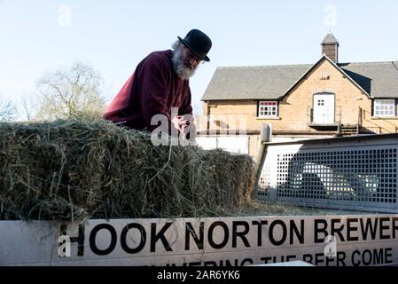 Roger Hughes, un drayman de 70 ans, décharge des balles de foin pour ses chevaux Shire dans Les Crochets familiaux de la brasserie Norton, fondée en 1849, dans le village Banque D'Images