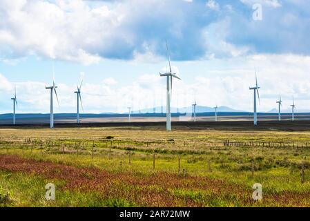 Éoliennes dans un champ herbacé avec des montagnes à l'horizon sur une journée de printemps partiellement nuageux Banque D'Images