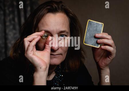 oncept: une femme mûre tient une petite boule de verre au niveau des yeux et carte de divination noire. Allégorie de magie, occultisme, divination Banque D'Images