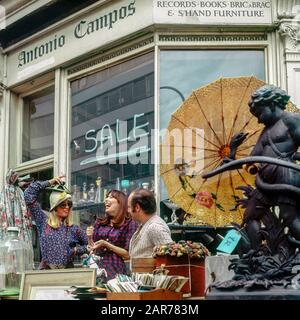 Londres années 1970, deux femmes s'amusant avec le marchand tout en faisant des achats à la boutique d'antiquités, Kensington, Angleterre, Royaume-Uni, GB, Grande-Bretagne, Banque D'Images