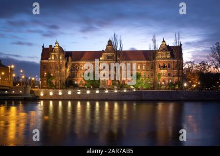Wroclaw, Pologne. Bâtiment historique lumineux du Musée national reflétant dans la rivière Oder au crépuscule Banque D'Images